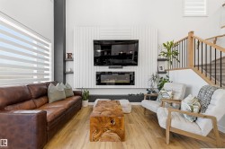 Spacious living area featuring light wood-finish flooring, a contemporary fireplace with shiplap-style surround, built-in shelving, and a natural wood staircase with black metal balusters - 