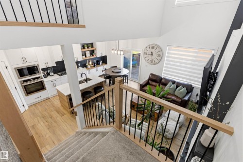 Open-concept living space featuring wood-finish flooring, a contemporary kitchen with white cabinetry and dark backsplash, a kitchen island with seating, built-in stainless steel appliances, and a vaulted ceiling - 7 Tenor Link, Spruce Grove, AB 