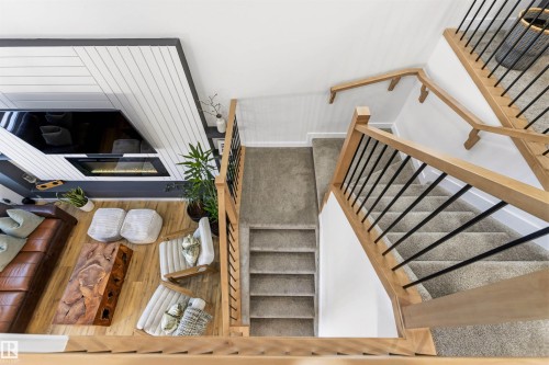 Multi-level interior featuring a contemporary fireplace with a decorative wood panel surround, wood-finish flooring, and a carpeted staircase with wood handrails and black metal balusters - 7 Tenor Link, Spruce Grove, AB 