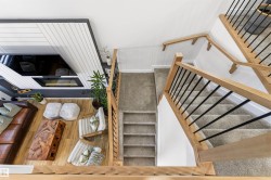 Multi-level interior featuring a contemporary fireplace with a decorative wood panel surround, wood-finish flooring, and a carpeted staircase with wood handrails and black metal balusters - 