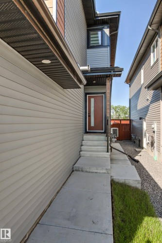 Contemporary exterior featuring horizontal siding, a prominent dark bronze front door with vertical glass insert, concrete walkway, and integrated soffit lighting - 7 Tenor Link, Spruce Grove, AB 