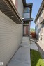 Contemporary exterior featuring horizontal siding, a prominent dark bronze front door with vertical glass insert, concrete walkway, and integrated soffit lighting - 7 Tenor Link, Spruce Grove, AB 
