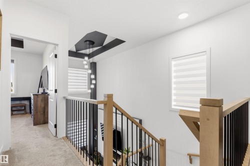 Upper-level hallway featuring light beige carpeting, a modern staircase with natural wood handrails and black metal balusters, and a contemporary pendant light fixture - 7 Tenor Link, Spruce Grove, AB 