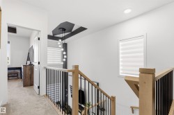 Upper-level hallway featuring light beige carpeting, a modern staircase with natural wood handrails and black metal balusters, and a contemporary pendant light fixture - 