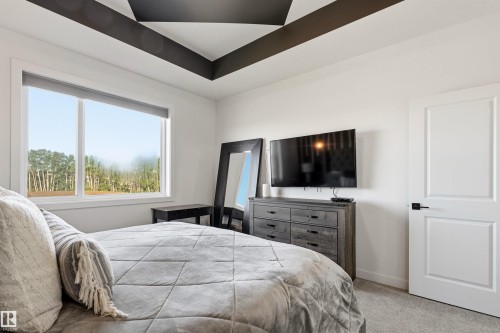 Bedroom featuring a tray ceiling with dark accent beams, a large window, light gray carpet, and a solid white door with dark hardware - 7 Tenor Link, Spruce Grove, AB 
