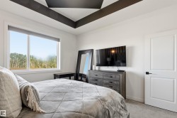 Bedroom featuring a tray ceiling with dark accent beams, a large window, light gray carpet, and a solid white door with dark hardware - 