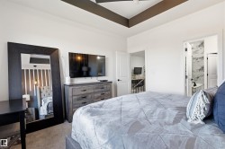 Bedroom featuring a recessed tray ceiling with accent paint, carpeted flooring, and a door opening to a bathroom with marble-patterned wall tile - 