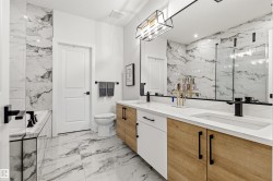 Contemporary bathroom featuring a dual vanity with wood-finish cabinetry, white countertops, and matte black fixtures - 
