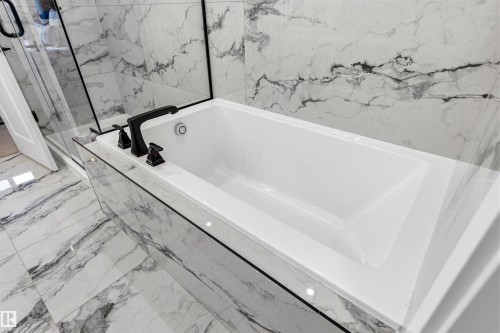 Built-in soaking tub with matte black fixtures, surrounded by large format tile with prominent veining - 7 Tenor Link, Spruce Grove, AB 