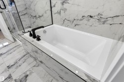 Built-in soaking tub with matte black fixtures, surrounded by large format tile with prominent veining - 