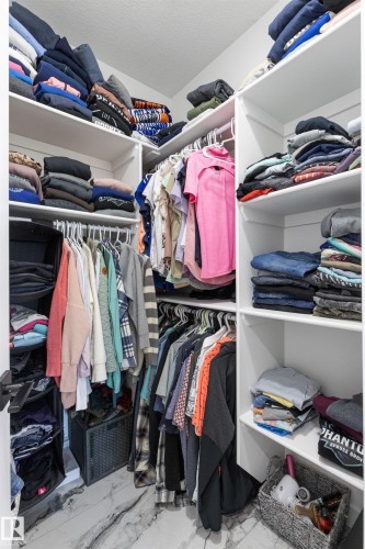 Walk-in closet featuring white built-in shelving, multiple hanging rods, and wood-finish flooring - 7 Tenor Link, Spruce Grove, AB 