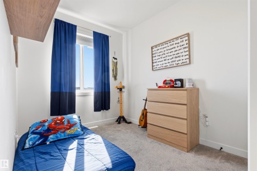 Bright room featuring a window with blue and dark blue curtains, a single floating wood-finish shelf, and light gray carpet - 7 Tenor Link, Spruce Grove, AB 
