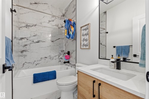 Bathroom featuring a white bathtub with a tile surround, a toilet, and a vanity with a white countertop - 7 Tenor Link, Spruce Grove, AB 