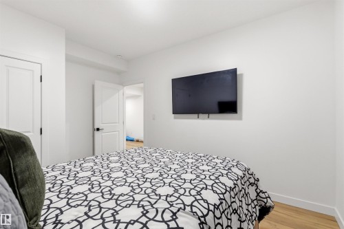 Wall-mounted television within a room featuring light wood-finish flooring, white walls, and white interior doors with dark hardware - 7 Tenor Link, Spruce Grove, AB 