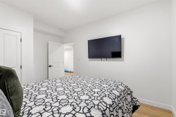 Wall-mounted television within a room featuring light wood-finish flooring, white walls, and white interior doors with dark hardware - 