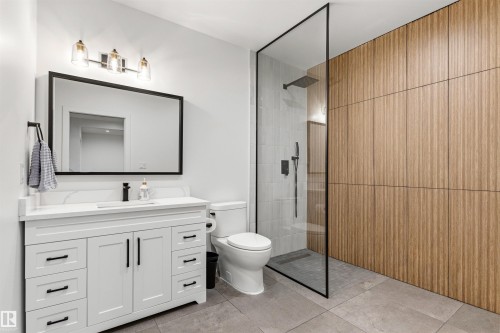 Modern bathroom featuring a glass-enclosed shower with rain showerhead, a white vanity with quartz-finish countertop, and a large framed mirror - 7 Tenor Link, Spruce Grove, AB 
