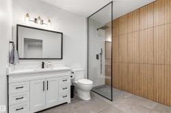 Modern bathroom featuring a glass-enclosed shower with rain showerhead, a white vanity with quartz-finish countertop, and a large framed mirror - 