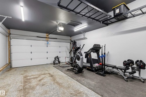 Spacious garage featuring a white overhead door, epoxy floor coating, recessed lighting, and overhead metal storage racks - 7 Tenor Link, Spruce Grove, AB 