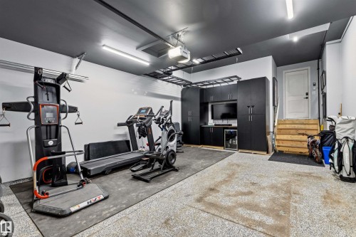 Dedicated fitness area featuring black cabinetry with a built-in television, wood stairs, and light-colored flooring - 7 Tenor Link, Spruce Grove, AB 