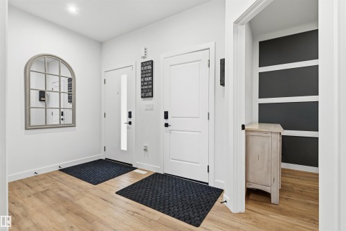 Foyer featuring wood-finish flooring, white doors with matte black hardware, and an arched window-pane mirror - 7 Tenor Link, Spruce Grove, AB 