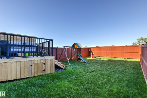 Expansive backyard featuring a manicured lawn, full privacy fencing, and a multi-level wood deck with black metal railings - 7 Tenor Link, Spruce Grove, AB 