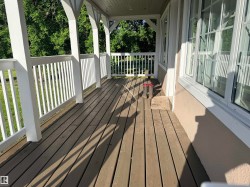Expansive covered porch featuring wood-finish decking, white balusters, and substantial support columns - 