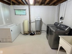 Utility area featuring exposed wood ceiling joists, a small window, painted concrete walls, and a utility sink - 