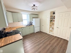 Kitchen featuring light green cabinetry, wood-finish countertops, a white subway tile backsplash, and wood-finish flooring - 