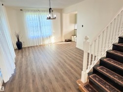 Spacious interior featuring wood-finish flooring, a contemporary chandelier, and a prominent staircase with dark treads and white balusters - 