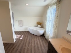 Bright bathroom featuring a freestanding soaking tub, wood-finish flooring, a vanity with an integrated sink, and recessed lighting - 