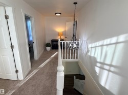 Upper-level hallway featuring plush carpeting, a modern drum pendant light fixture, and a white baluster railing - 