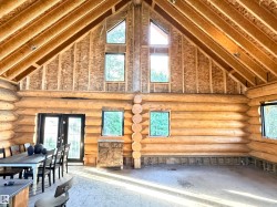 Vaulted ceiling with exposed wood beams, log wall construction, multiple windows, double French doors, and an open concept layout - 