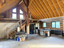 Vaulted ceiling with exposed wood beams, log wall construction, natural wood staircase, kitchen island with seating, and a black refrigerator - 