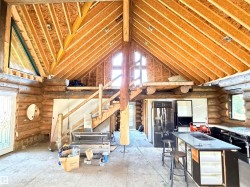 Vaulted ceiling with exposed wood beams, log wall construction, multi-level design, main level kitchen area with island seating, and a prominent staircase - 