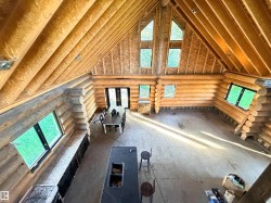 Soaring vaulted ceilings with exposed beams, log wall construction, multiple large windows, and a partially installed kitchen island with an integrated sink - 