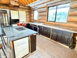 Rustic kitchen featuring log wall construction and exposed wood ceiling beams - 