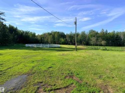 Expansive green space featuring a white round pen, wood fencing, and mature trees bordering the property - 