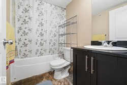 Full bathroom featuring a white tub, toilet, and a dark wood-finish vanity with an undermount sink and dark countertop - 