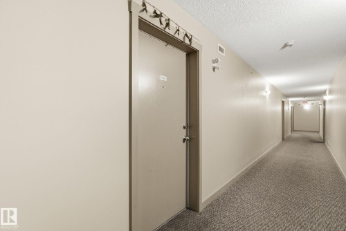 Long hallway with textured carpeting, cream-painted walls, and ceiling-mounted light fixtures - 424 1510 Watt Drive, Edmonton, AB 