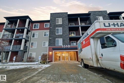Multi-story building featuring a stone facade, multiple balconies with dark railings, a prominent main entrance, and diverse exterior siding colors - 424 1510 Watt Drive, Edmonton, AB 