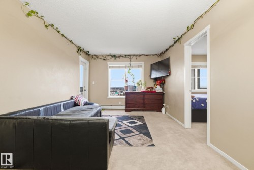 Living area featuring neutral wall tones, carpeted flooring, a window offering natural light, and an open doorway to an additional room - 424 1510 Watt Drive, Edmonton, AB 