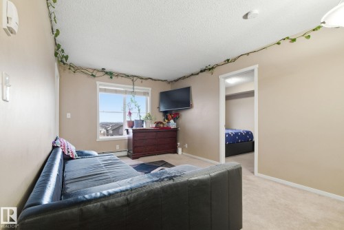 Carpeted interior space featuring a window with exterior visibility, light beige wall paint, a white ceiling, and a doorway opening to an additional room - 424 1510 Watt Drive, Edmonton, AB 