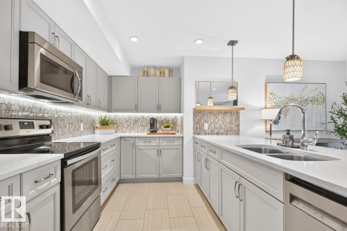 Modern kitchen featuring light gray cabinetry, stainless steel appliances, and light-toned wood-finish flooring - 207 5025 Edgemont Boulevard, Edmonton, AB 