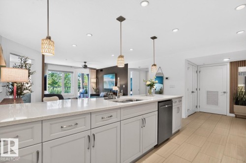 Spacious kitchen island featuring a light-toned countertop, integrated sink, and stainless steel dishwasher - 207 5025 Edgemont Boulevard, Edmonton, AB 