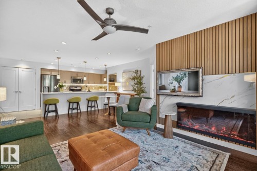 Open-concept living area featuring a modern linear fireplace with a marble-look surround, a wood-slat accent wall, and wood-finish flooring - 207 5025 Edgemont Boulevard, Edmonton, AB 