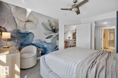 Accent wall featuring abstract floral wallpaper, wood-finish dresser with a glass top, and a ceiling fan with integrated lighting - 207 5025 Edgemont Boulevard, Edmonton, AB 