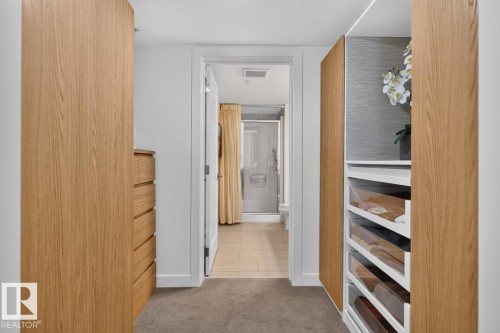 Walk-in closet featuring integrated wood-finish cabinetry, built-in dresser, and organized shelving with pull-out drawers - 207 5025 Edgemont Boulevard, Edmonton, AB 