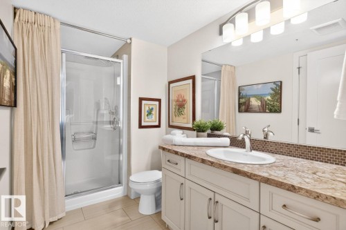 Bathroom featuring a glass-enclosed shower, a vanity with a light-toned countertop, a rectangular undermount sink, and a mirrored wall with a multi-bulb light fixture - 207 5025 Edgemont Boulevard, Edmonton, AB 