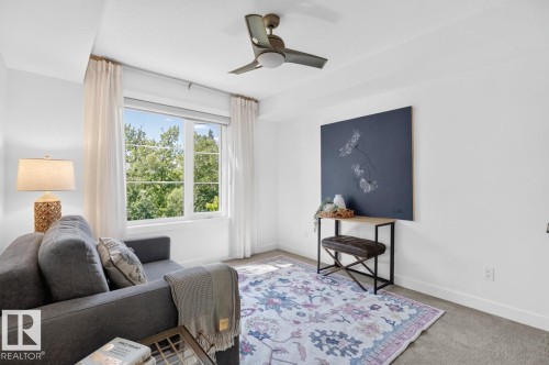 Bright interior room featuring a large multi-pane window, flush-mounted ceiling fan, and carpeted flooring - 207 5025 Edgemont Boulevard, Edmonton, AB 