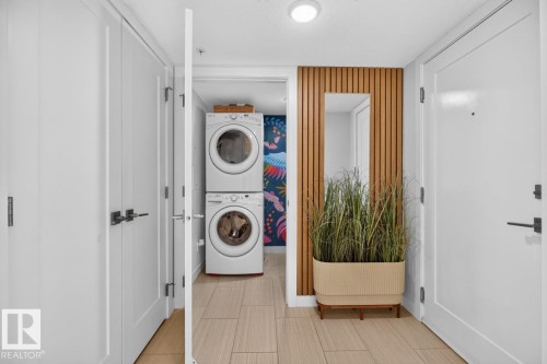 Entryway featuring light-toned tile flooring, white doors with contemporary hardware, and a wood-slat accent wall with an integrated mirror - 207 5025 Edgemont Boulevard, Edmonton, AB 